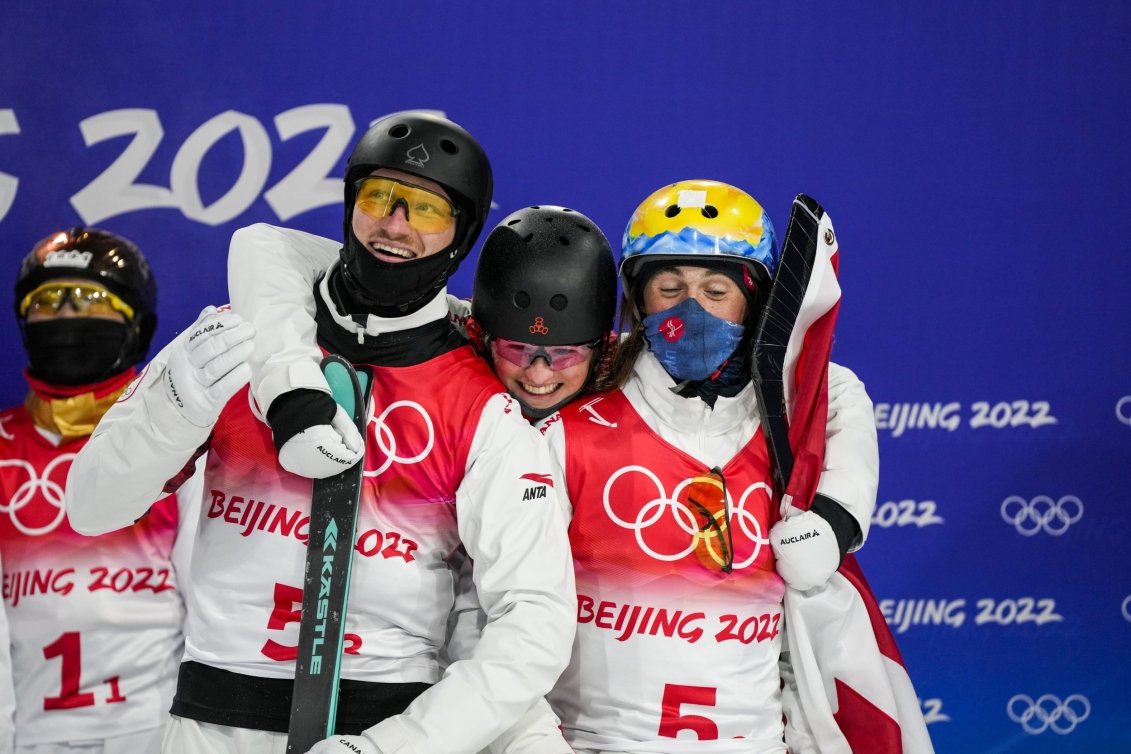 Three Canadian aerialists happily hug as they hear their scores