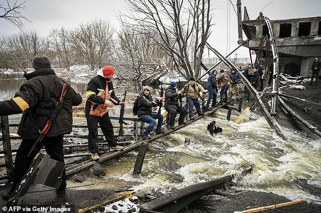 Members of an Ukrainian civil defense unit pass new assault rifles to the opposite side of a blown up bridge on Kyiv's northern outskirts, where fighting with Russian forces has been taking place