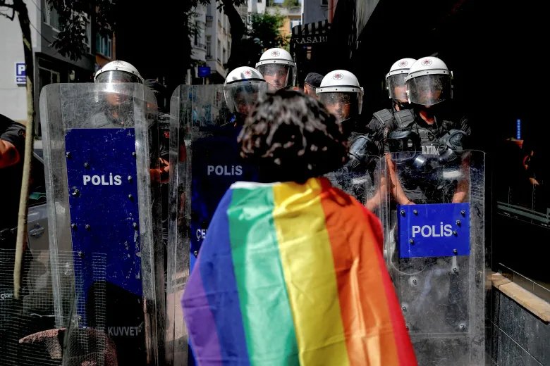 TOPSHOT - A participant faces riot policemen wearing a rainbow flag during a Pride march in Istanbul, on June 26, 2022. - Turkish police forcibly intervened in a Pride march in Istanbul, detaining dozens of demonstrators and an AFP photographer, AFP journalists on the ground said. The governor's office had banned the march around Taksim Square in the heart of Istanbul but protesters gathered nearby under heavy police presence earlier than scheduled.