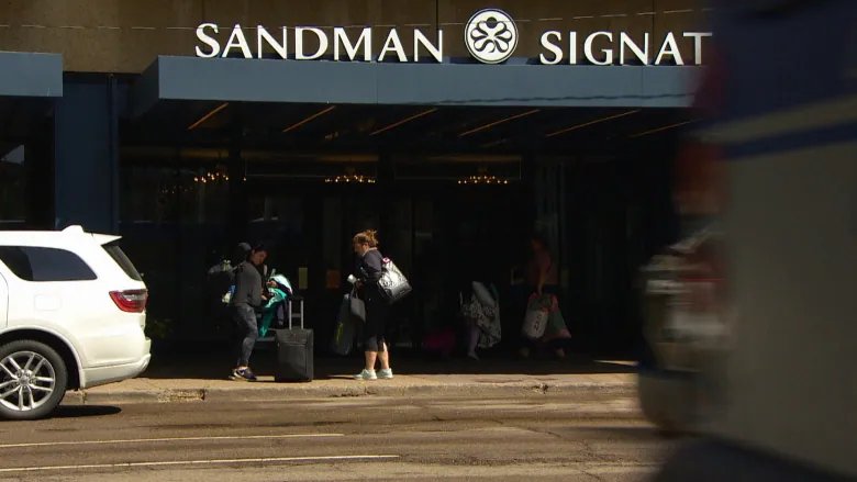 People with luggage stand near the front of a hotel.