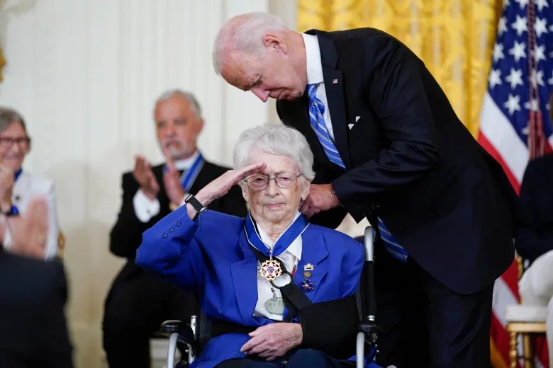 A man puts a medal around the neck of a woman in a wheelchair, who is saluting. 