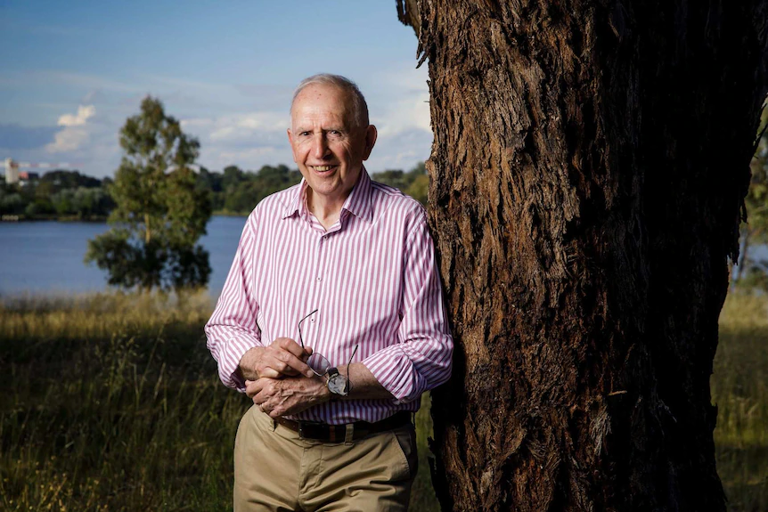 An elderly man leaning against a tree and smiling.