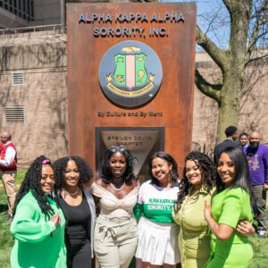 Sorority sisters wearing green stand in front of a large pillar honoring the Alpha Kappa Alpha Sorority, Inc.